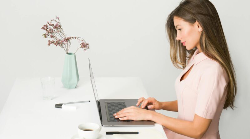 A woman in a pink dress working on a laptop at a modern, minimalist desk.