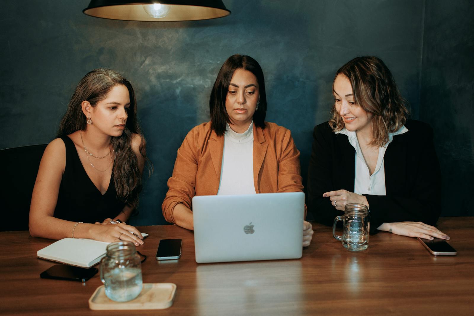 Three women engaged in a work discussion around a laptop in a professional setting.